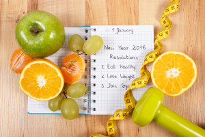 New years resolutions eat healthy, lose weight and join gym written in notebook, fresh fruits, dumbbells for fitness and tape measure, healthy lifestyle